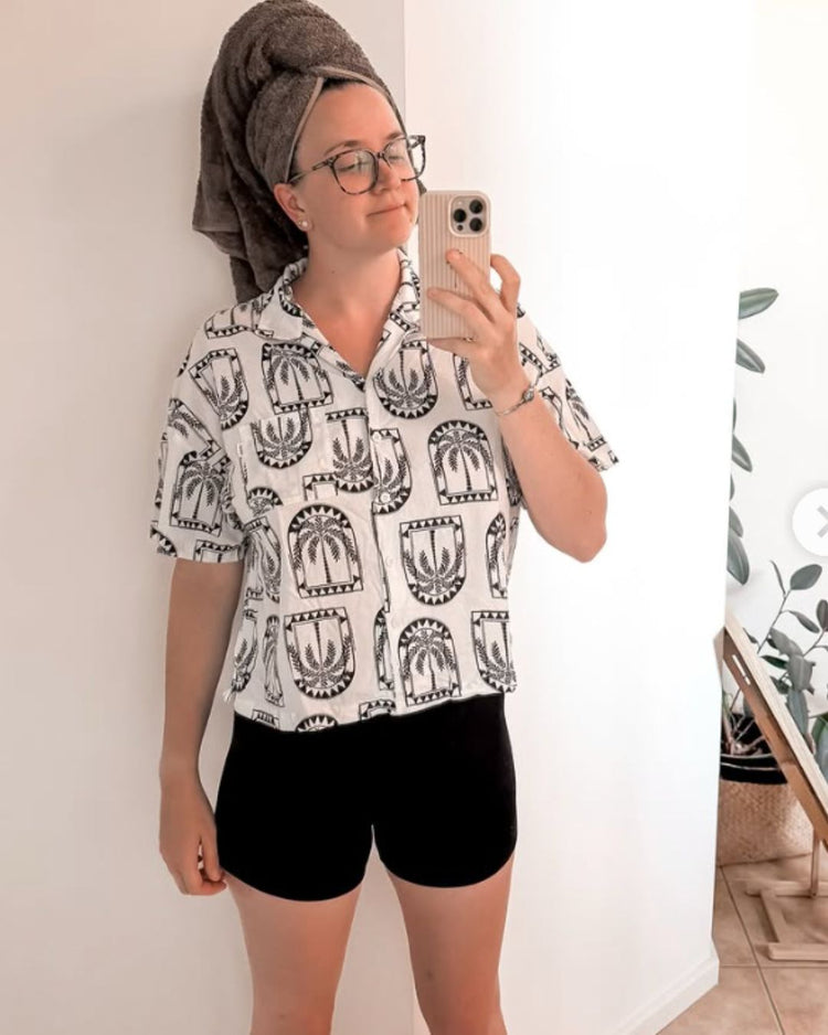 Person wearing a patterned shirt and Fri Period boxer briefs, standing in a room with a chair and plant.