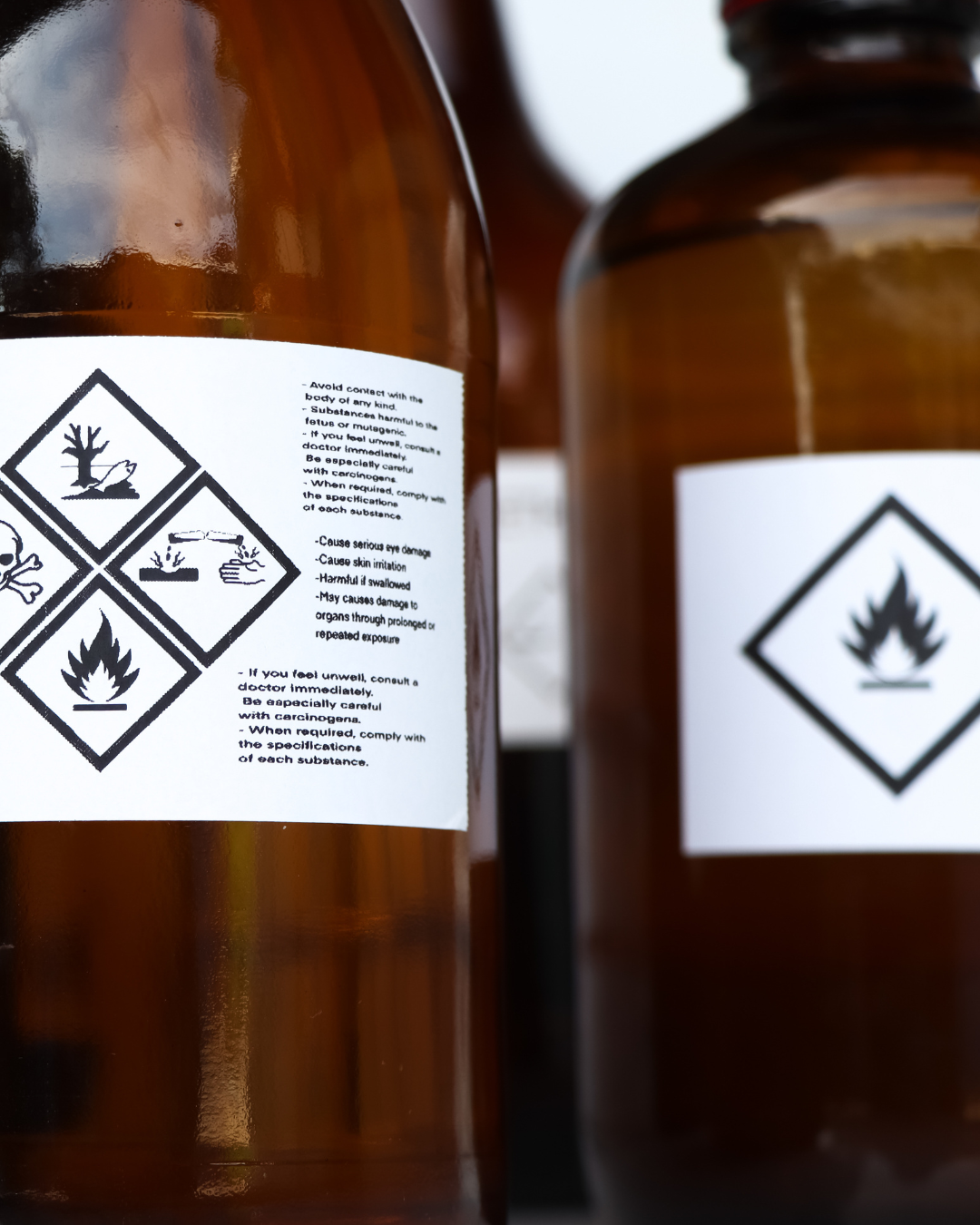 Two brown bottles with hazardous material labels featuring warning symbols.