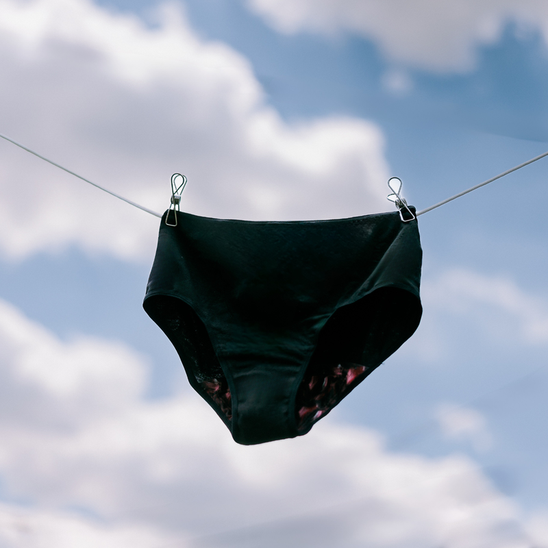 Black underwear hanging on a clothesline against a blue sky with clouds