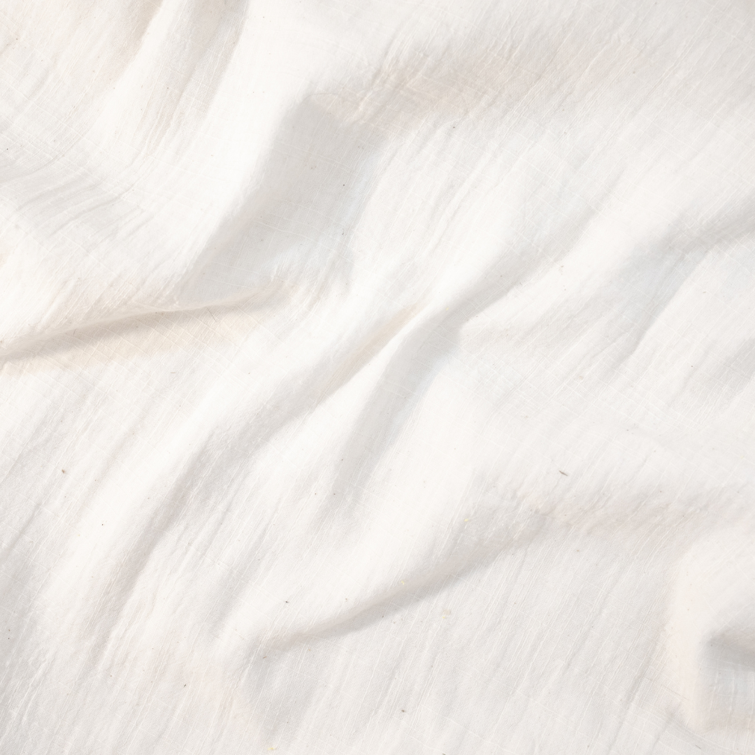 A close-up of white textured fabric with soft folds and a slightly crinkled surface.
